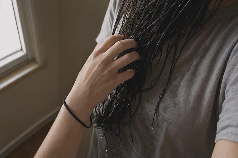 Cabelo molhado solto sobre o ombro, mão passando os dedos entre os fios, elástico parado no pulso